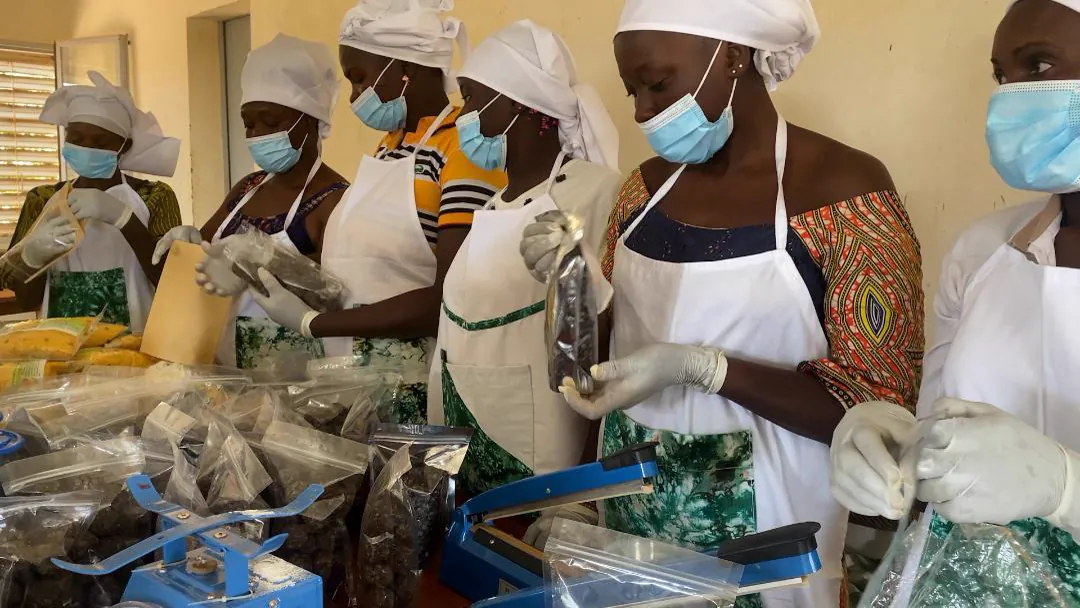 Femmes en tablier et masque conditionnant des produits transformés.