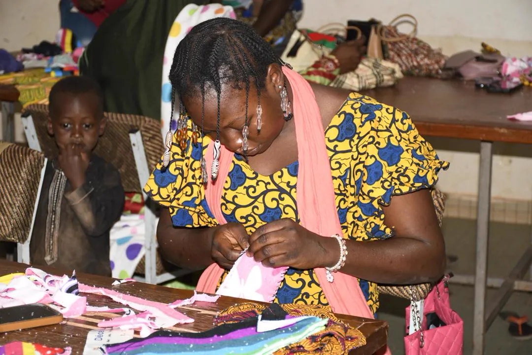 Une femme confectionne des articles en tissu lors d'un atelier, un enfant à ses côtés.